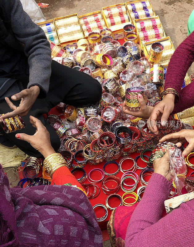印度新德里街头市场上，印度印度教妇女的手卖五颜六色的手镯，游客坐在地板上选择Connaught Place商店的彩色彩虹手镯和金色手镯